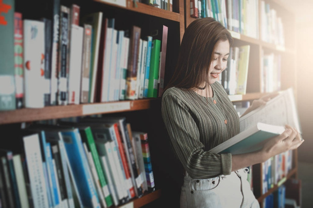 Genç kadın librar içinde kitap ve stand açık bookshelf okuma - Fotoğraf, Görsel