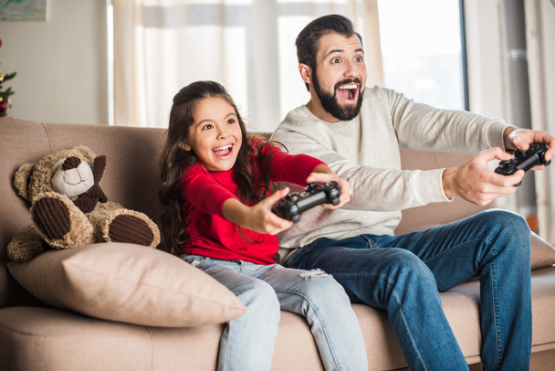 excited father and daughter playing video game at home - Photo, Image