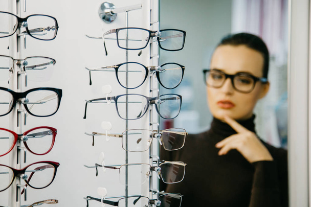 Stand with glasses in the store of optics. Beautiful girl in glasses on a background. Selective focus - Fotoğraf, Görsel