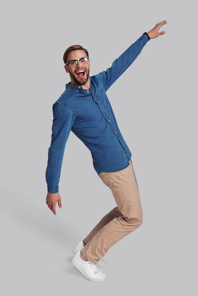 Full length of playful young man dancing and smiling in studio - Foto, afbeelding
