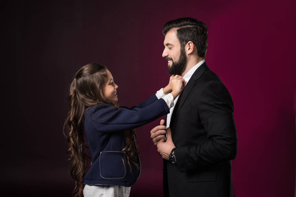 daughter fixing father tie and looking at each other on burgundy - Fotoğraf, Görsel