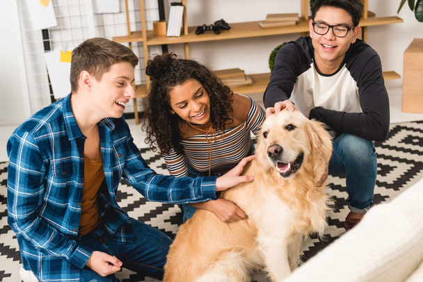 happy multiethnic teens palming dog at home - Photo, Image