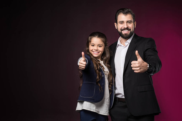 Улыбающиеся отец и дочь показывают большие пальцы на бордовом
 - Фото, изображение