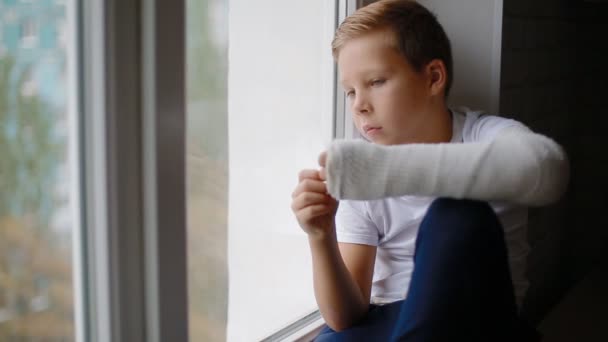 Sad boy with broken hand looking at the window - Footage, Video