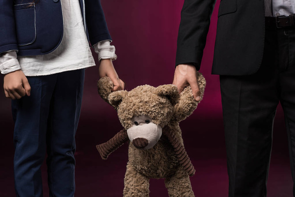 cropped image of daughter and father holding teddy bear on burgundy - Photo, Image