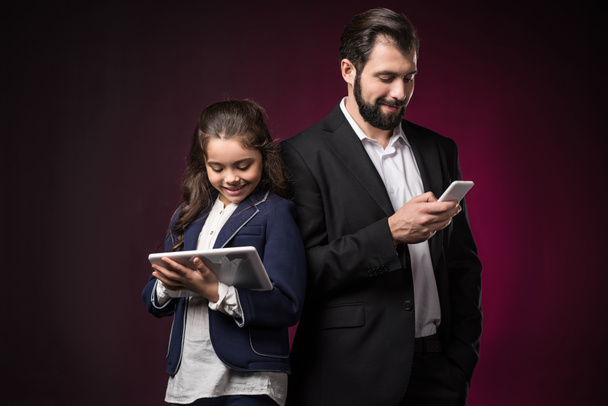 father and daughter using tablet and smartphone on burgundy - Фото, зображення