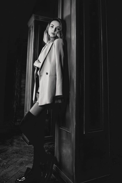 Black and white portrait of young attractive pretty blonde woman in the  jacket, leather shirt, gaiters, patent shoes on the dark background - Zdjęcie, obraz