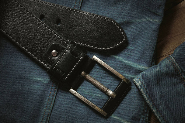 black leather belt and blue denim jacket. Fashionable casual clothing and accessories closeup, top view, vintage style - Photo, Image
