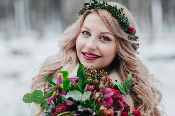 Face of a smiling girl of Slavic appearance with a wreath. Beautiful bride holds a bouquet in winter background. - Valokuva, kuva