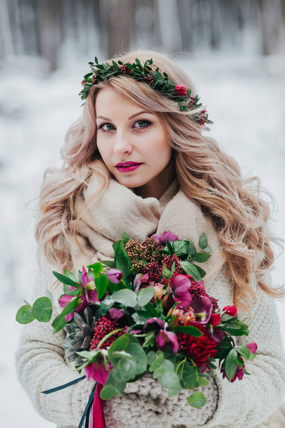 A young girl of Slavic appearance with a wreath of wildflowers. Beautiful bride holds a bouquet in winter background. - Foto, immagini