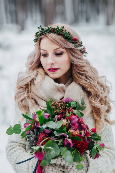 A young girl of Slavic appearance with a wreath of wildflowers. Beautiful bride holds a bouquet in winter background. - Photo, image
