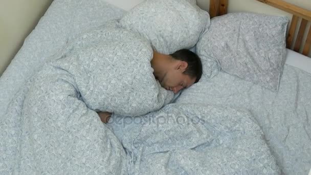 Jongeman is zoet slapen in bed in een foetushouding op zijn zijaanzicht van bovenaf - Video