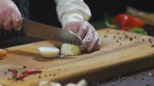 De chef-kok snijdt UI. Uien als ingrediënt voor het maken van soep of een andere schotel. Bovenaanzicht Slow motion - Video