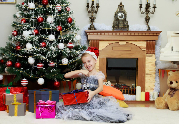 Little girl sitting near Christmas tree with a big gift. - Foto, afbeelding