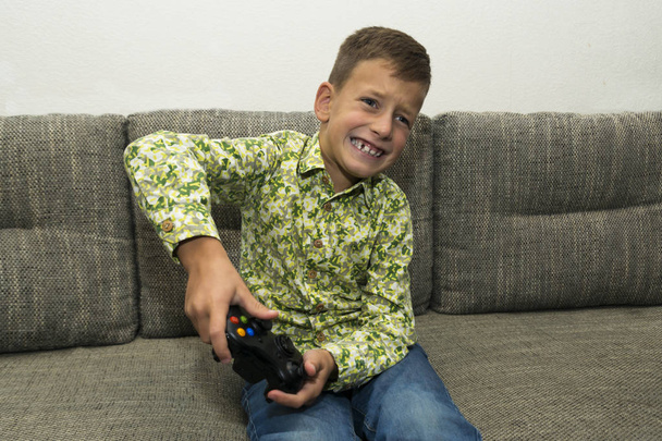 Мальчик играет в видеоигры с джойстиком, сидя на диване
 - Фото, изображение