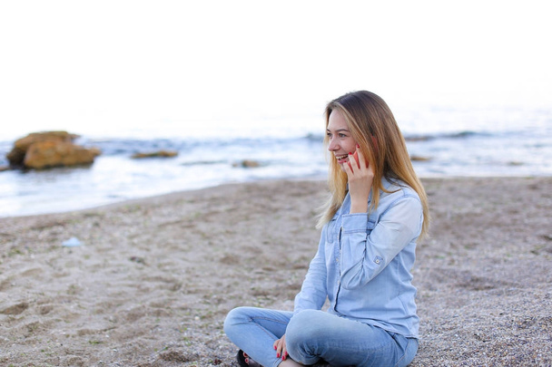 Gyönyörű nő beszél a mobil mosollyal, és ül a strandon-n - Fotó, kép