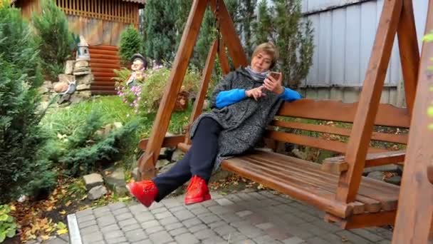 Usmívající se žena v módní oblečení houpe na lavičce - Záběry, video