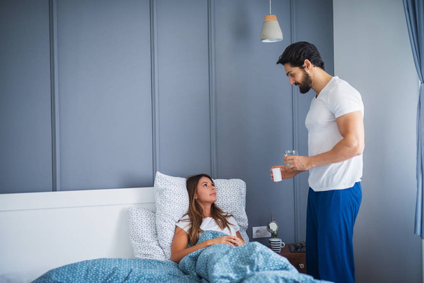 careful handsome young man bringing medications to ill girlfriend lying in bed - Fotografie, Obrázek