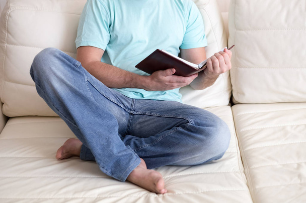 Un hombre leyendo un viejo libro de notas con las manos en el sofá blanco. Estilo de vida doméstico. Concepto educativo
. - Foto, Imagen