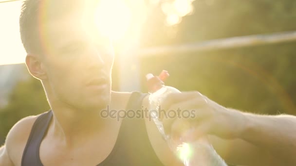 Muscular sportsman drinking water, training on stadium in sunset rays, slow-mo - Séquence, vidéo
