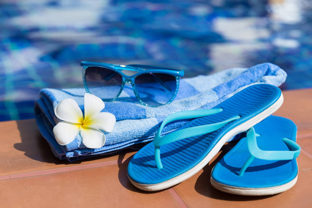 Blue slippers, sunglasses and towel on border of a swimming pool - Fotó, kép