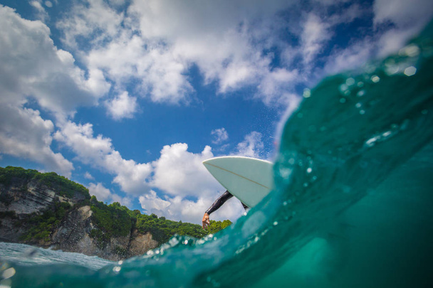 Surfer riding big blue wave on white board, half underwater split shot  - Foto, afbeelding