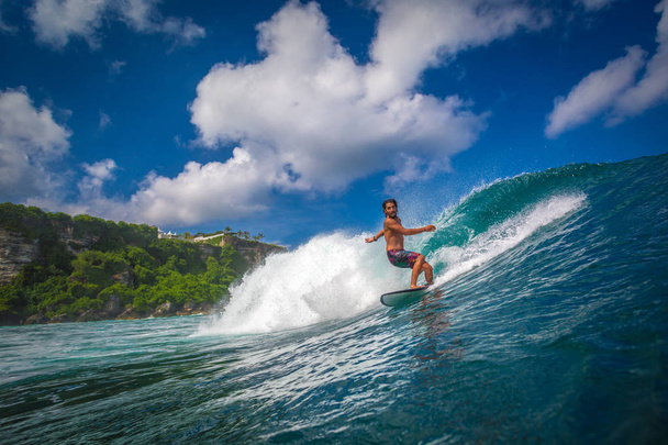 Indonesia, Bali, July 22 2016: A surfer riding big blue ocean wave - Foto, afbeelding
