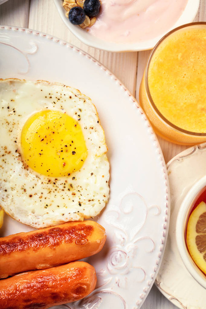 Breakfast of sunny side up eggs, sausages, orange juice, and fru - Photo, Image