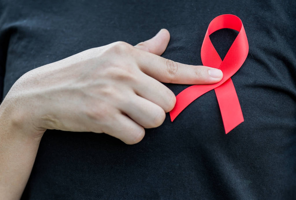 Manos de mujer sosteniendo cinta roja de conciencia del SIDA. Campaña de sensibilización sobre el sida
 - Foto, Imagen