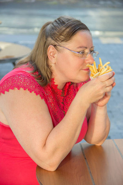 Толстая женщина ест гамбургер с фаст-фудом и картошку фри в кафе
 - Фото, изображение