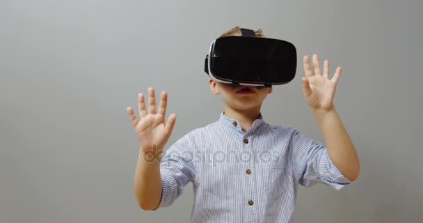 Portrait of the small funny boy using VR glasses and touching something in front of him on the grey wall background. VR set. Indoor - Materiał filmowy, wideo