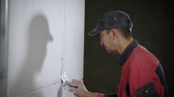 A young man who works as a builder puts a white grout on the joints between the tiles, he uses a spatula - Filmagem, Vídeo