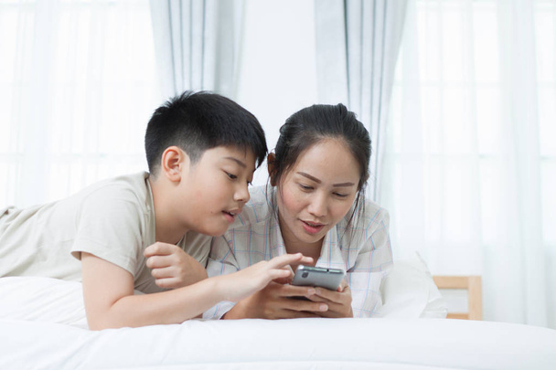 Asiatico donna con asiatico ragazzo guardando televisione su letto
. - Foto, immagini