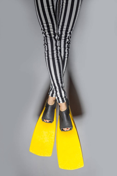 Woman wearing yellow flippers over gray background - 写真・画像