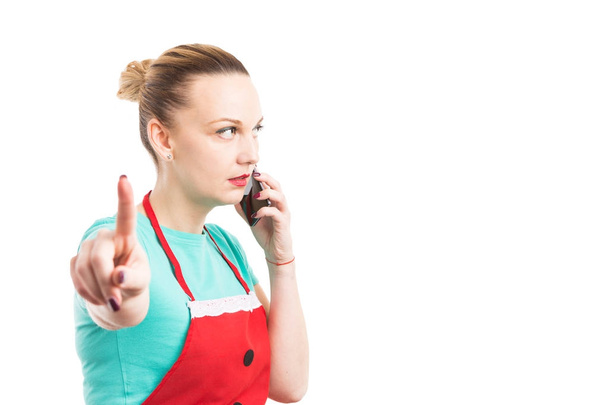 Esposa vistiendo delantal rojo sosteniendo el teléfono y haciendo espera gestur
 - Foto, Imagen