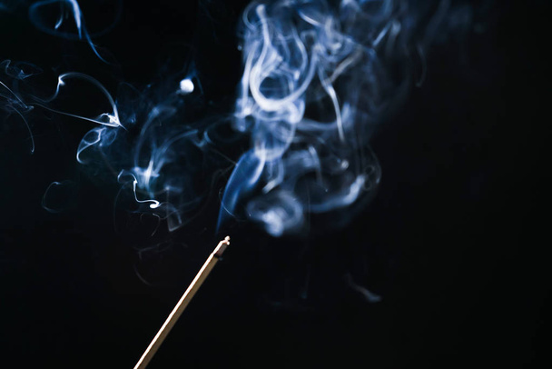 on a black background a lighted smoldering aroma stick, blue smoke - Фото, зображення