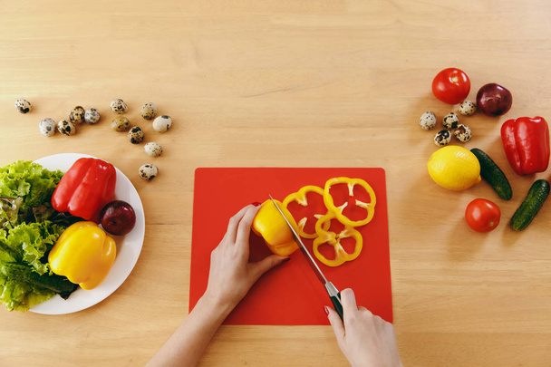 Una giovane donna taglia il pepe giallo per insalata con un coltello in cucina. Il concetto di dieta. Uno stile di vita sano. Cucinare a casa. Preparate il cibo. Vista dall'alto
. - Foto, immagini