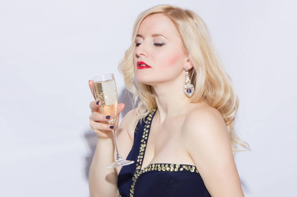 Studio portrait of a beautiful young blonde woman in a blue long evening dress. A girl is holding a glass of champagne in her hand - Foto, afbeelding