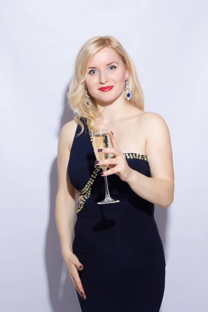 Studio portrait of a beautiful young blonde woman in a blue long evening dress. A girl is holding a glass of champagne in her hand - Photo, Image