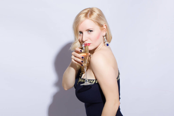 Studio portrait of a beautiful young blonde woman in a blue long evening dress. A girl is holding a glass of champagne in her hand - Foto, Bild
