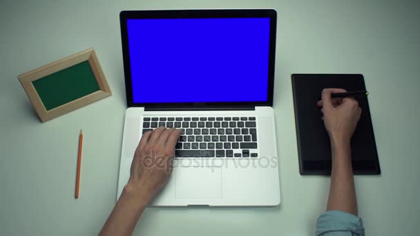Beyaz masa yeşil ekranlı dijital grafik sekmesini ve dizüstü bilgisayar kullanan adam - Video, Çekim
