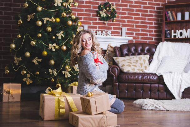 Beautiful happy girl unfolding a Christmas gift box on a holiday in the morning in a beautiful room room. The girl is open a Christmas gift near the decorated Christmas tree. Concept of winter holiday - Фото, зображення