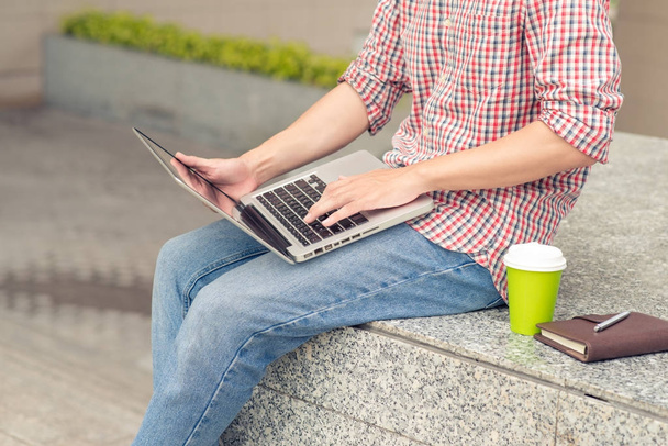 Jeune homme assis avec ordinateur portable à l'extérieur de l'immeuble de bureaux
 - Photo, image
