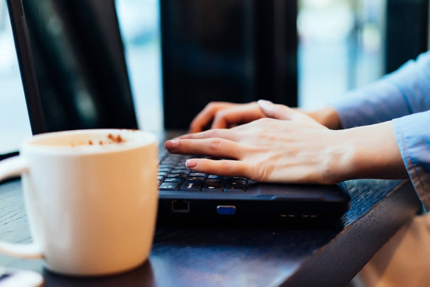 фрилансерша, работающая в кафе за ноутбуком, рядом с кружкой с ароматным кофе
 - Фото, изображение