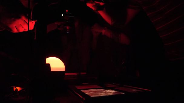 Exposure of the image onto sensitized paper using photographic enlarger in darkroom. Woman working in a red dark room - Photo, Image