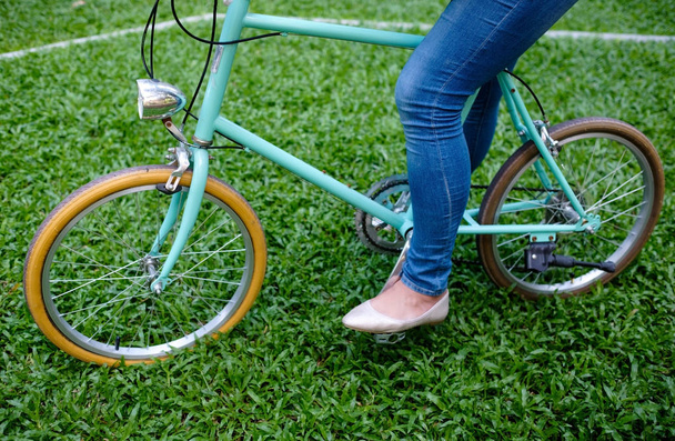 Blue bicycle of vintage style standing on green grass with woman in jeans. - Foto, afbeelding