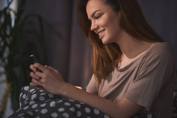 Nuori kaunis nainen käyttää puhelinta, kun makaa sängyssä
 - Valokuva, kuva