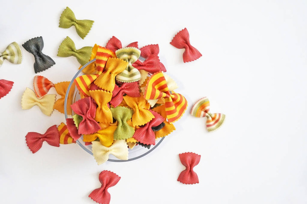 Funny multicolored pasta. Beautiful pasta in the form of a butterfly. Original Italian pasta isolated on white background. Iridescent curly pasta on a white background in a transparent plate. - 写真・画像