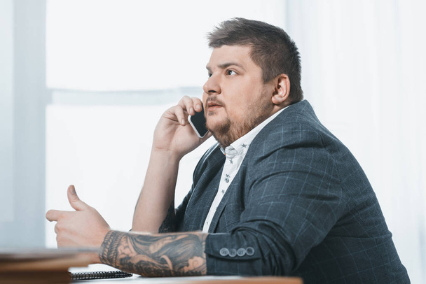 fat businessman talking on smartphone in office - Fotó, kép