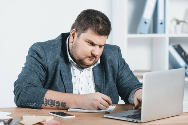 overweight businessman in suit writing and working with laptop at workplace - Foto, afbeelding